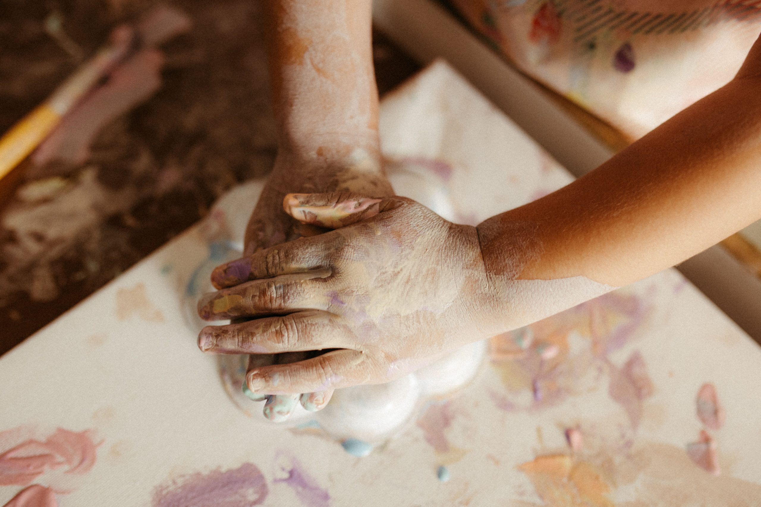 Close-up of a child's hands sculpting colorful clay art on a table indoors.