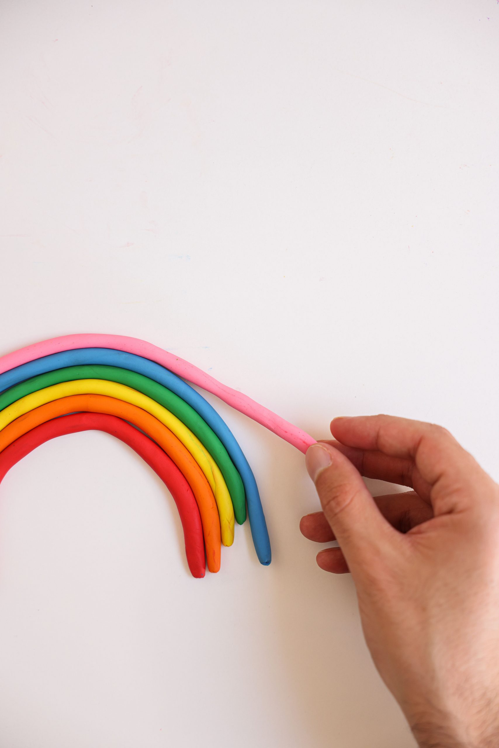 Hand arranging colorful clay rainbow on a white background.